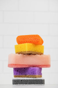 Multicolored sponges for washing dishes are stacked on a white tiled background.