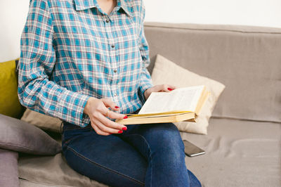 Midsection of man reading book while sitting on sofa at home