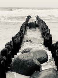 Wooden posts on rock at sea shore against sky