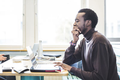 Side view of young male student using laptop at table in university cafeteria