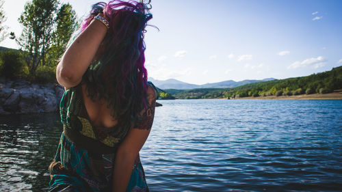 Rear view of young woman standing by river against sky