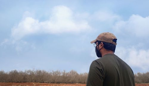 Rear view of man standing on field against sky