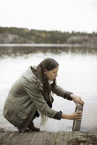 Side view of woman opening thermos at lakeshore