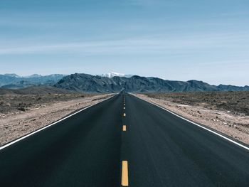 Empty road by mountains against sky