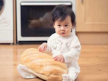 Cute baby girl sitting with bread on hardwood floor at home