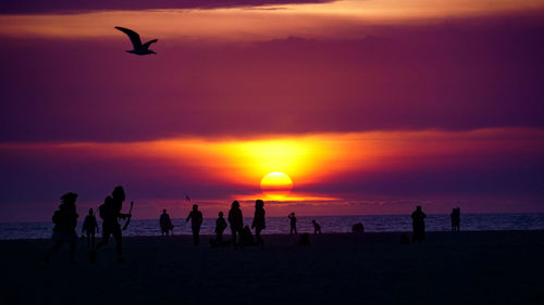 Silhouette people on calm beach at sunset