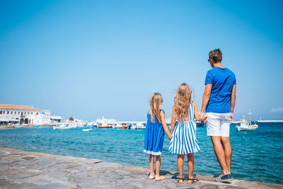 Rear view of friends standing at sea against blue sky