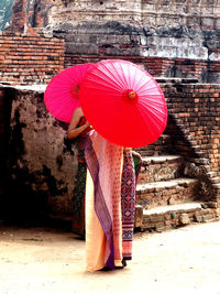 Woman holding umbrella standing against brick wall