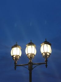 Low angle view of illuminated street light against blue sky