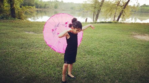 Full length of girl holding umbrella while standing on field
