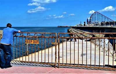 Rear view of man standing by railing against sea