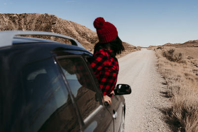 Spain, navarre, female tourist leaning out of car window over dirt road in bardenas reales