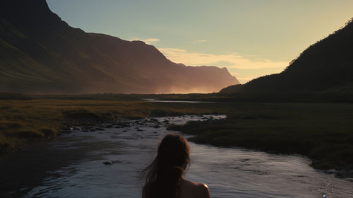 Rear view of woman standing at lakeshore during sunset