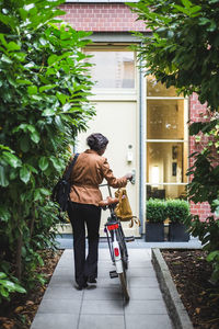 Rear view of female architect with bicycle standing against house