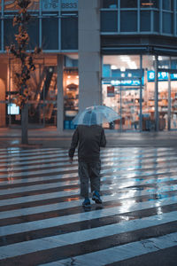 Rear view of man walking on street during rainy season