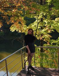 Portrait of young woman standing by railing against trees