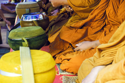 Midsection of monks praying while sitting by baskets