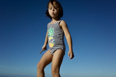 Low angle view of girl standing against clear blue sky