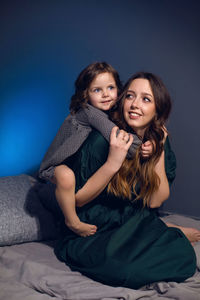 Mother and daughter in dresses sitting on a bed in a bedroom with a blue wall