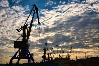 Silhouette cranes against sky at sunset