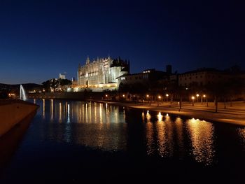 Illuminated buildings by river against sky at night