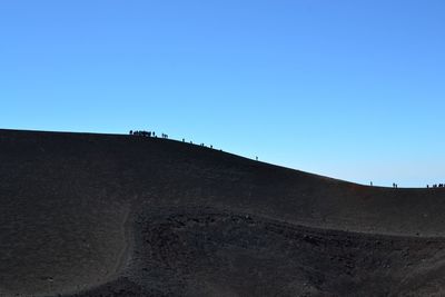 Low angle view of sand dunes against clear blue sky