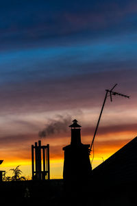 Low angle view of silhouette chimney against dramatic sky during sunset