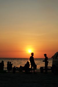 Silhouette friends standing at beach against sky during sunset