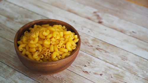 Uncooked dry macaroni pasta in a wooden bow on a rustic wooden table.