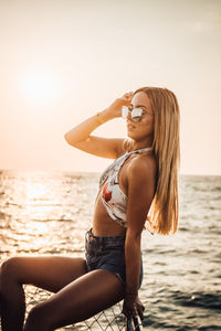 Young woman with arms raised on beach against sky