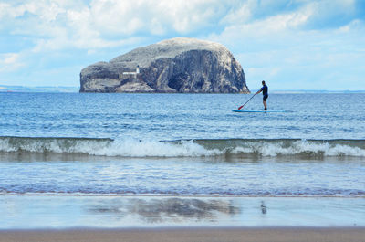Man paddleboarding on sea against sky