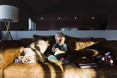 Cute girl yawning while eating bread on sofa at home