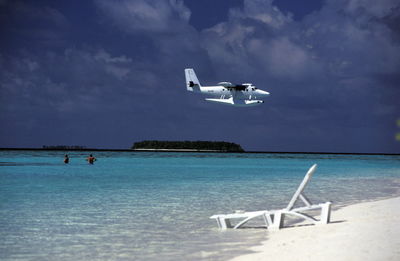 Seaplane flying over sea against cloudy sky