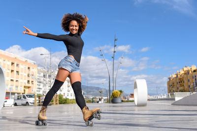 Full length of young woman with roller skates on town square against sky