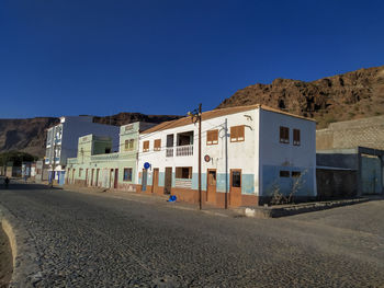 Road by buildings against clear blue sky