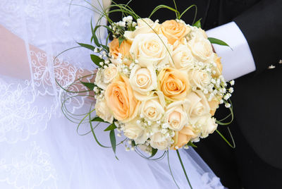 Midsection of bride and groom holding bouquet during wedding