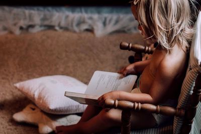 High angle view of girl reading book while sitting on chair at home