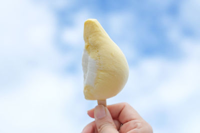 Cropped hand of woman holding popsicle stick against sky