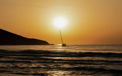 Scenic view of sailing boat on sea against orange sky during sunrise