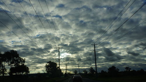 Low angle view of silhouette electricity pylons against sky at sunset