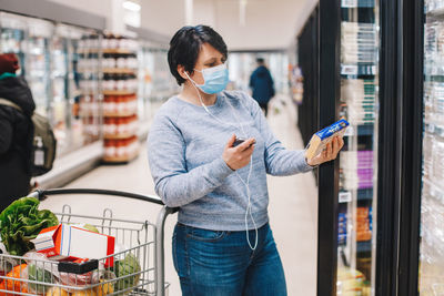 Middle age brunette woman shopping in grocery store supermarket and talking on audio chat phone. 