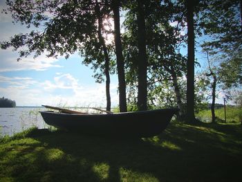 Boat moored at grassy field by lake against sky