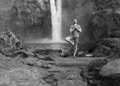 Full length of man meditating while standing against waterfall