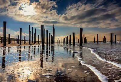 Wooden posts on beach against sky during sunset