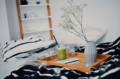 Green smoothie by flower vase in tray on decorated bed at home