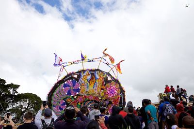 Crowd standing at amusement park against sky