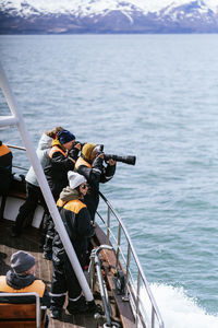 Side view of male and female travelers in protective clothes photographing and admiring seascape during cruise in modern boat on sunny day in iceland