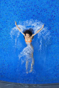 Young woman splashing water while swimming in pool