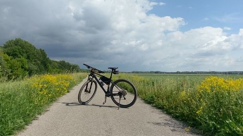 Bicycle on road amidst field against sky