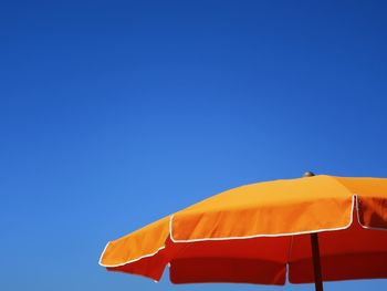 Low angle view of parasol against clear blue sky